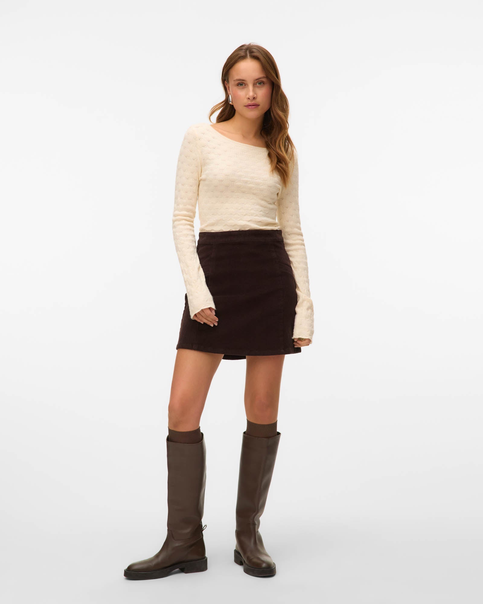 Woman wearing a cream sweater, brown skirt, and brown knee-high boots on a white background